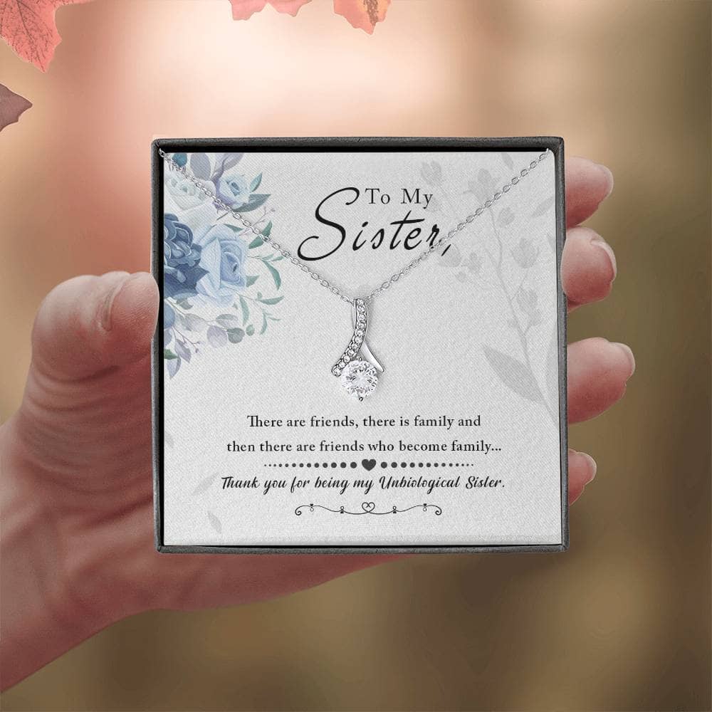A hand holding the Alluring Beauty Necklace, a stunning gift with a petite ribbon-shaped pendant in 14k white gold or 18k yellow gold finish. Pendant dimensions: 0.8" height / 0.4" width. Adjustable length: 18" - 22". Packaged in a soft touch box for easy gifting.