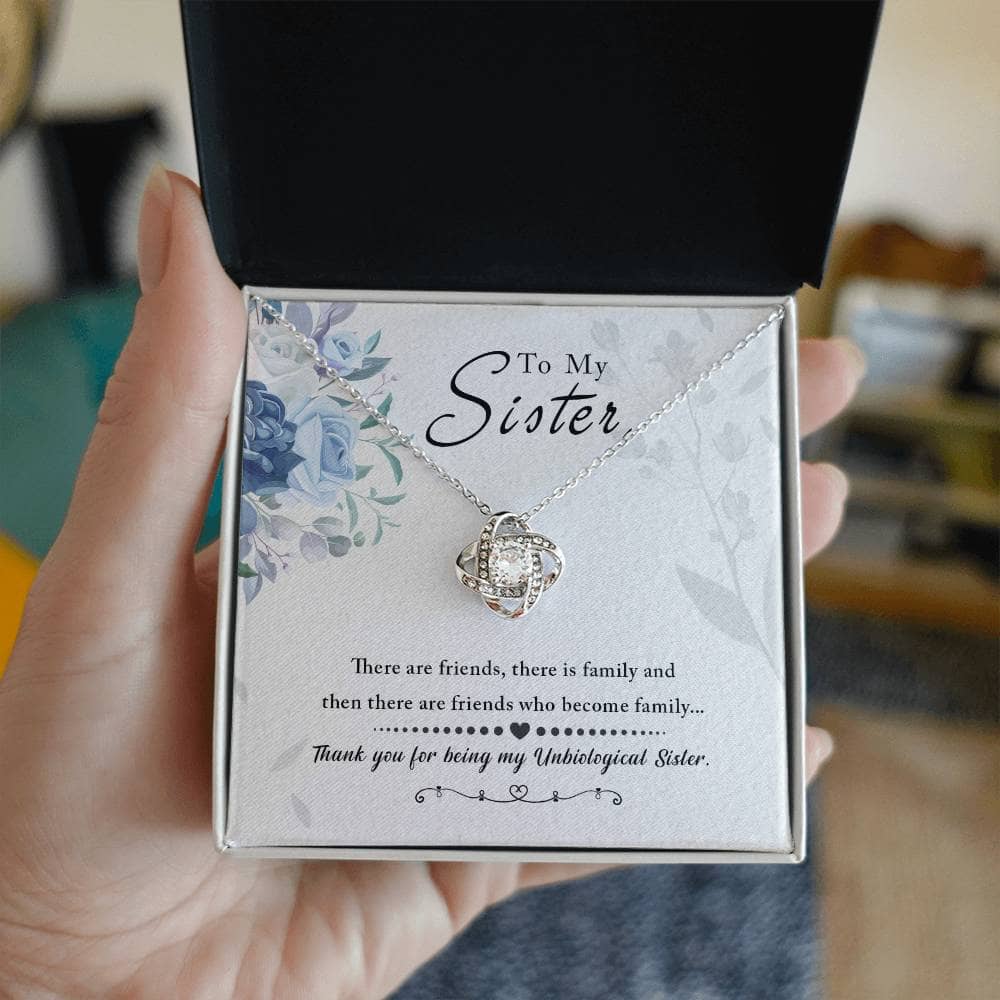A hand holding a Personalized Unbiological Sisters Necklace in a box, showcasing the exquisite love knot pendant design.
