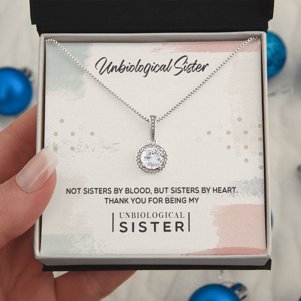 A hand holding a Personalized Unbiological Sisters Necklace in a box, symbolizing the unique bond between sisters.