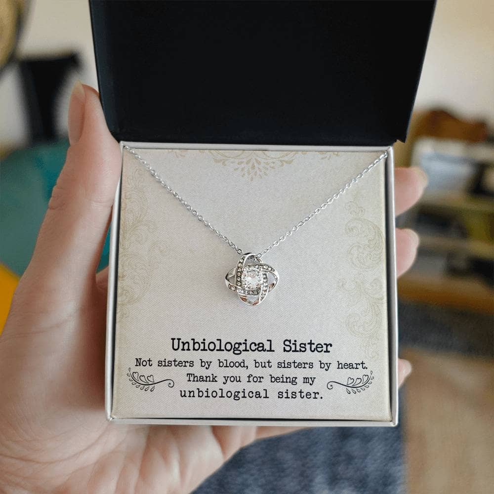 A hand holding a Custom Unbiological Sisters Love Knot Necklace in a box, symbolizing the enduring connection between unbiological sisters.