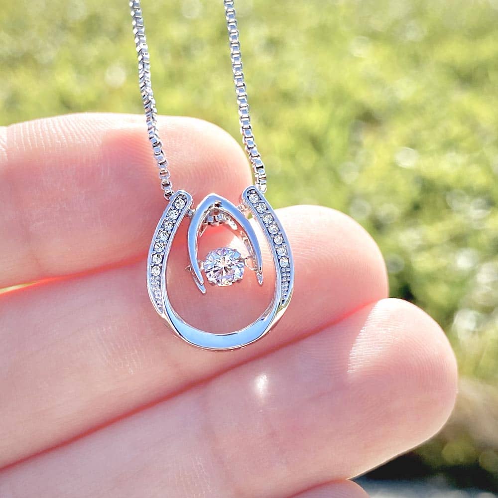 A hand holding a personalized Unbiological Sisters Necklace, featuring an interlocking heart pendant and adjustable chain.