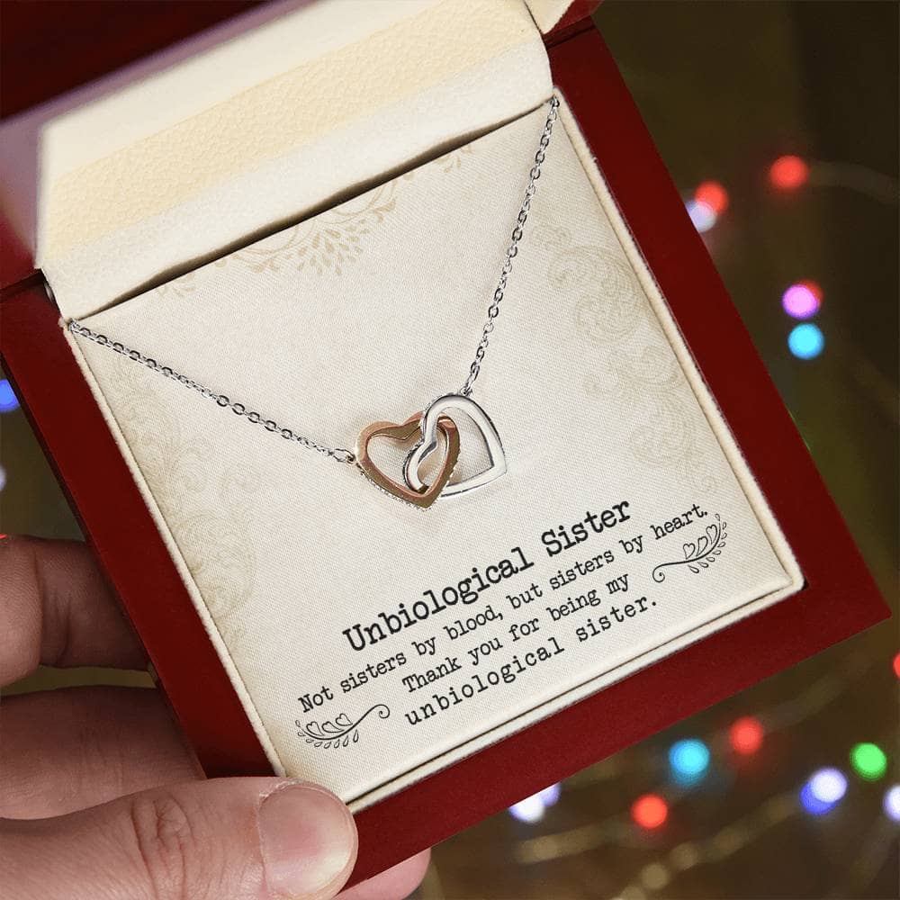 Alt text: "A hand holding a heart pendant necklace in a box, symbolizing the unbreakable bond of unbiological sisters. Personalized and crafted with 14k white gold or 18k gold finishes, adorned with luminescent cubic zirconia. A meaningful gift of love and companionship."