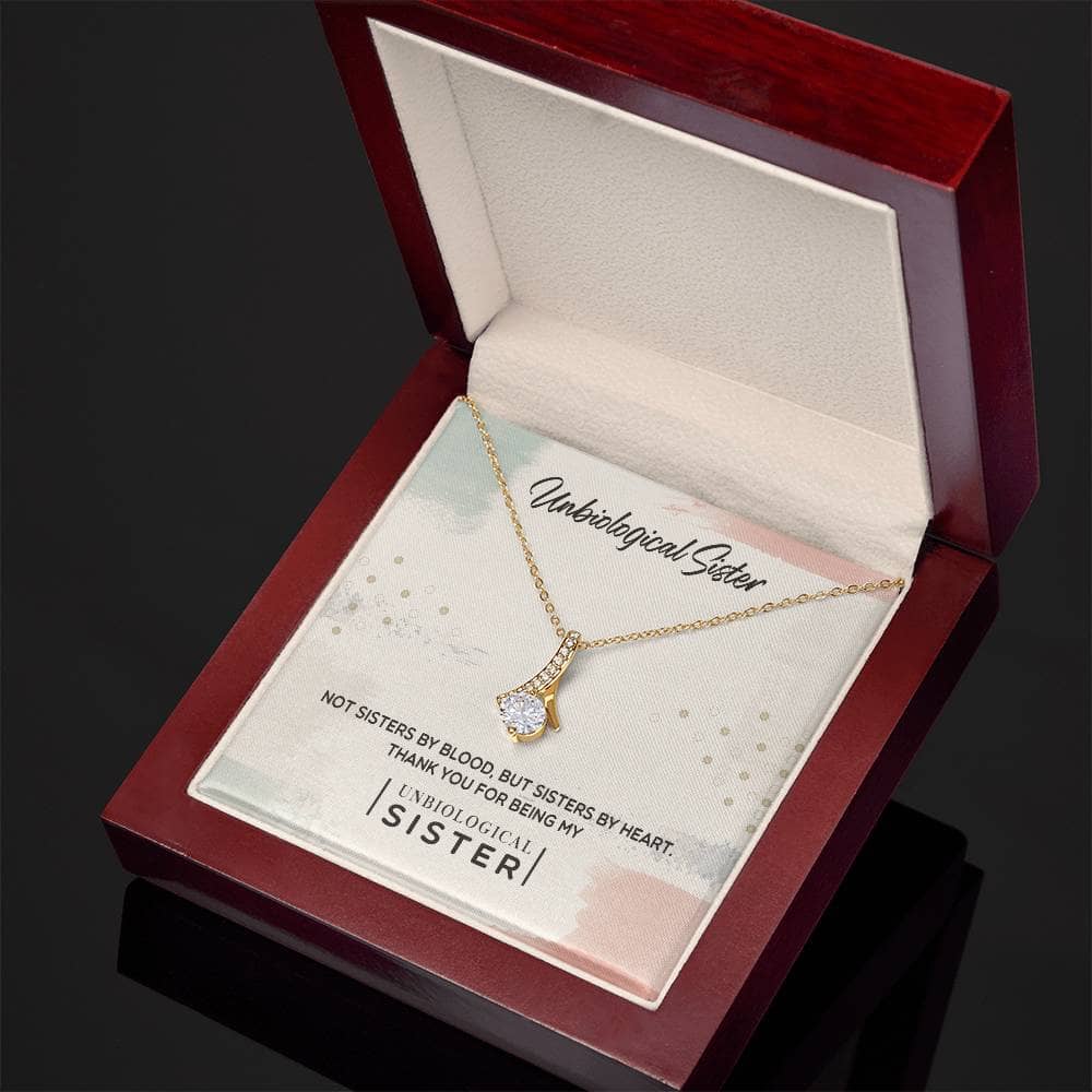 A gold necklace in a box, featuring a radiant cubic zirconia cushion-cut on a heart or knot pendant. Celebrate sisterhood with this customizable Unbiological Sisters Love Knot Necklace.