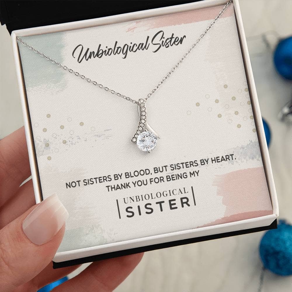A hand holding a Customizable Unbiological Sisters Love Knot Necklace, adorned with a radiant cubic zirconia pendant. Celebrate sisterhood with this elegant piece crafted in 14k white gold or 18k gold finish.