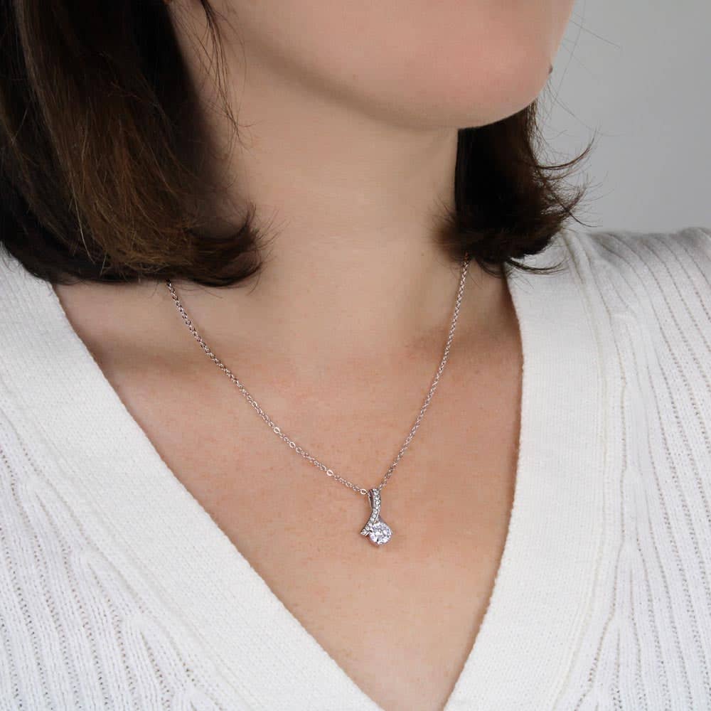 A woman wearing a Customizable Unbiological Sisters Love Knot Necklace, featuring a radiant cubic zirconia cushion-cut pendant in 14k white gold or 18k gold finish.