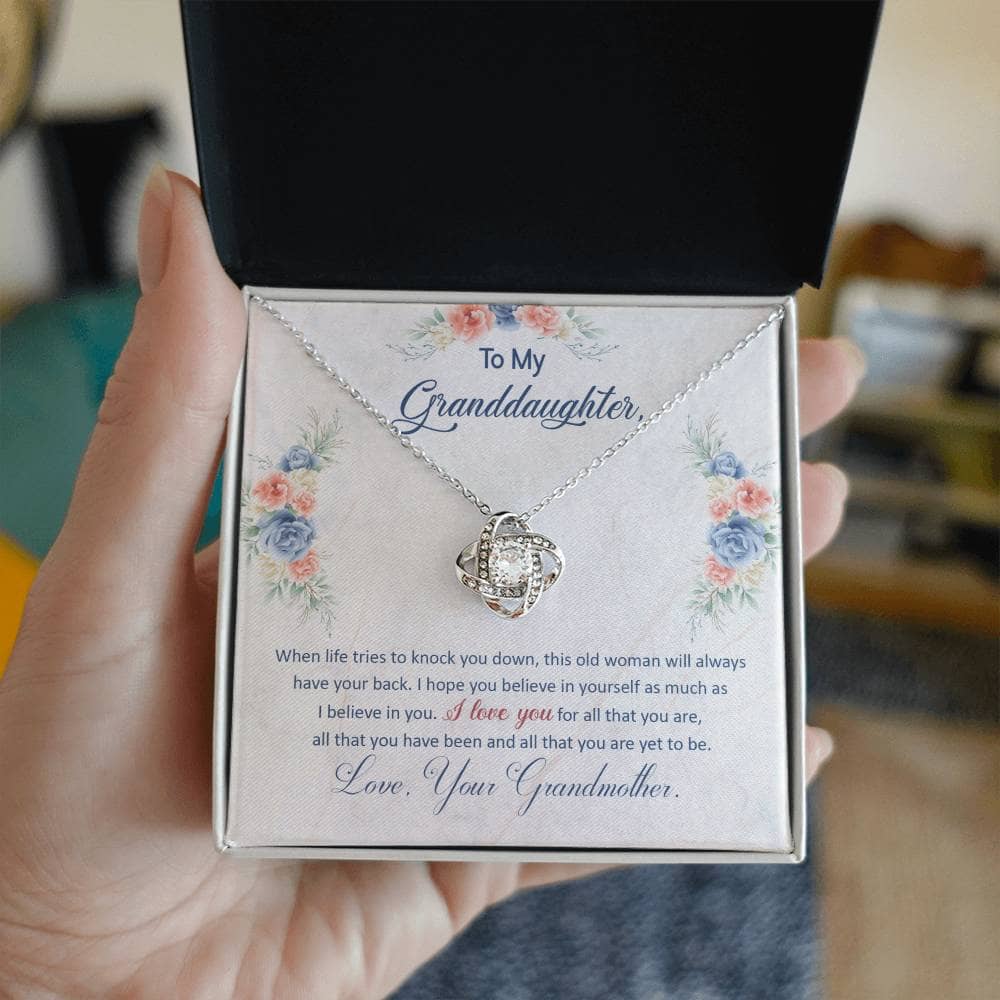 A hand holding a Customized Granddaughter Love Knot Necklace in a luxurious box with LED lighting.