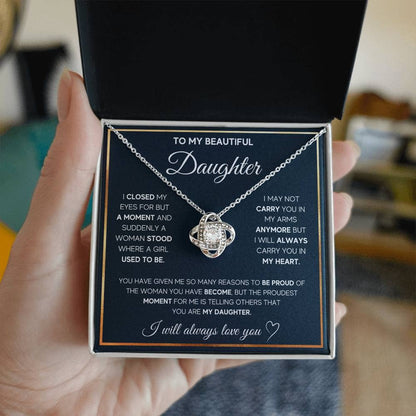 A hand holding an Elegant Personalized Daughter Necklace with a heart pendant and cubic zirconia, packaged in a luxurious mahogany-inspired box with LED lighting.
