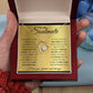 Alt text: "A hand holding a personalized Soulmate Necklace with a heart-shaped pendant on a gold chain in a box"