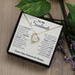 Alt text: "A personalized Soulmate Necklace with intertwined hearts and a note on a wood surface, symbolizing eternal love."