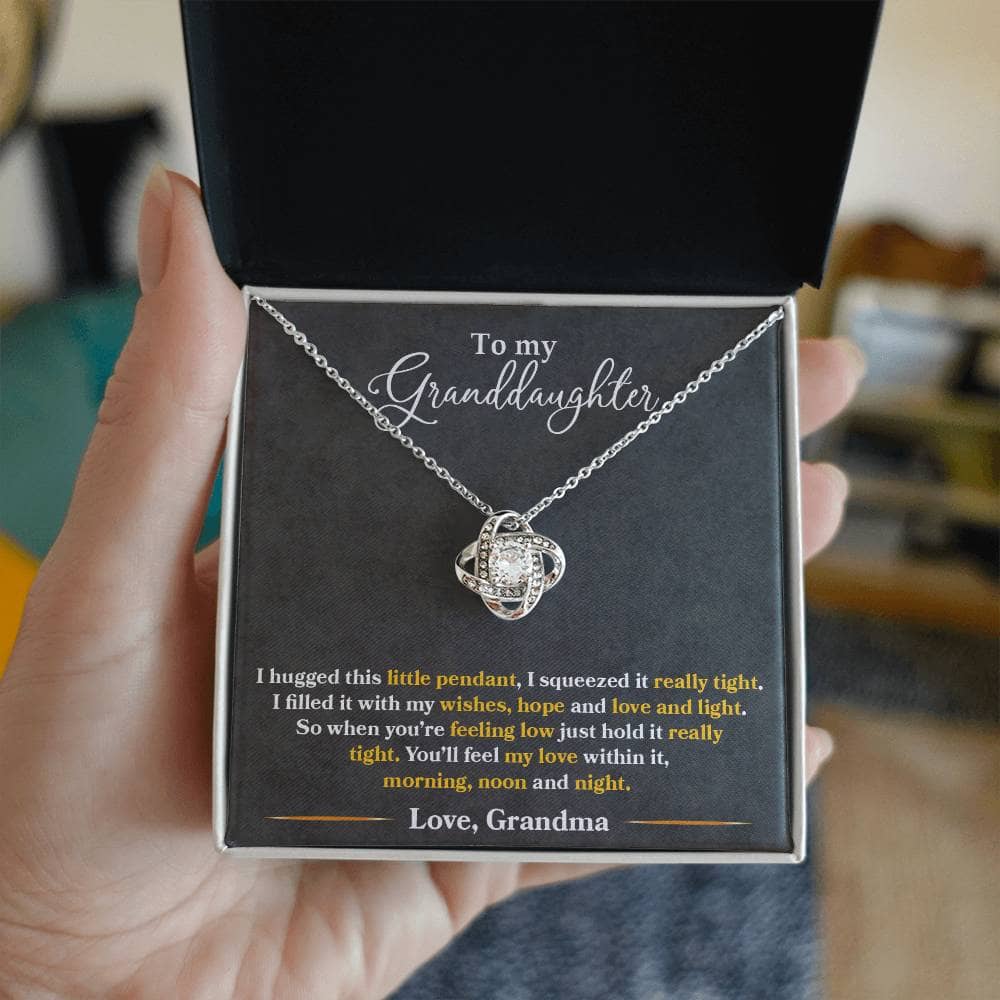 Alt text: "A hand holding the Love Knot Necklace in a box, showcasing a silver necklace with a large stone, symbolizing the enduring bond between grandparents and granddaughters."