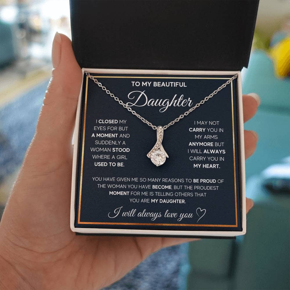 Alt text: "A hand holding a personalized daughter necklace with an elegant heart pendant in a box"