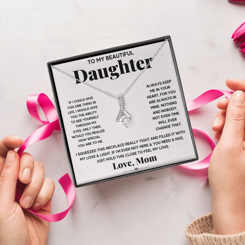Alt text: "Hands holding a box with a personalized daughter necklace and pink ribbon"