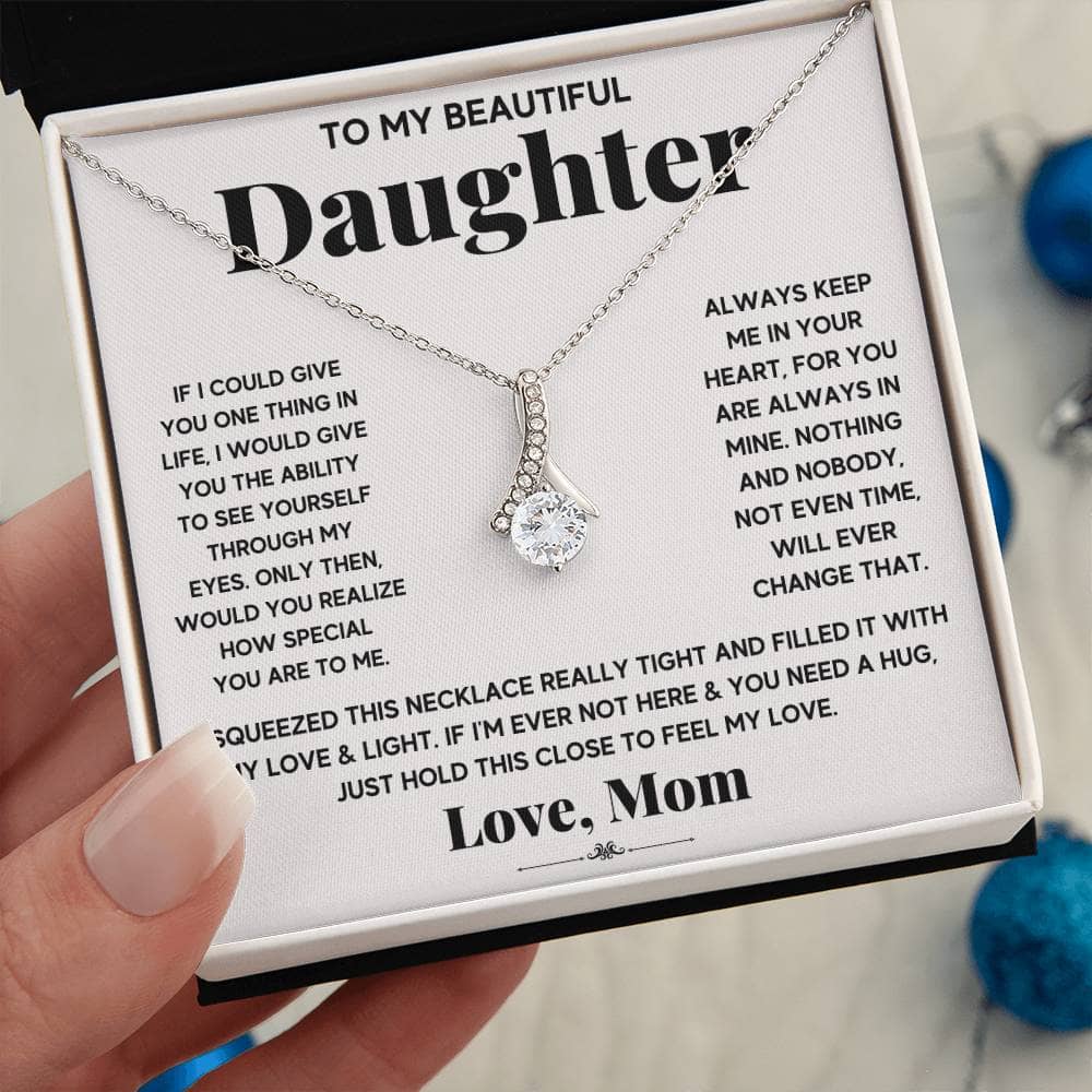 A hand holding a Personalized Daughter Necklace, an elegant symbol of parental love, featuring a heart-shaped pendant and a cushion-cut cubic zirconia. The necklace arrives in a luxurious mahogany-style box with LED lighting for a magical unboxing experience.