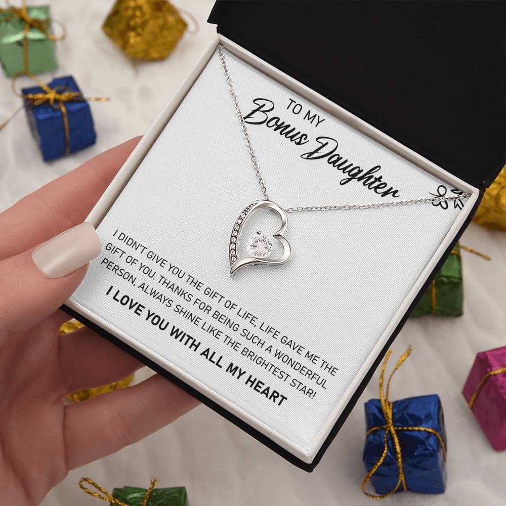 Alt text: "A hand holding a personalized daughter necklace in a box, showcasing a heart-shaped pendant with a sparkling cubic zirconia. The necklace represents unbreakable parent-daughter bonds."