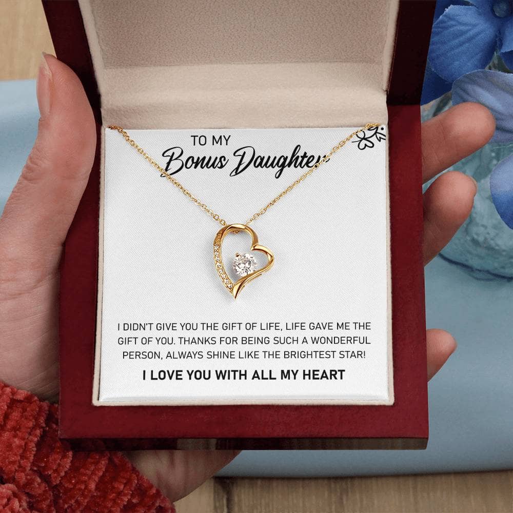 A hand holding a personalized daughter necklace in a box, featuring a heart-shaped pendant with a diamond in the middle.