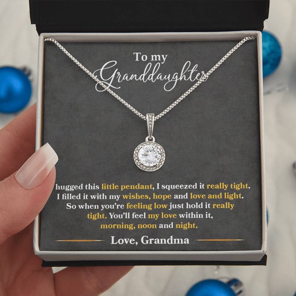 A hand holding a Personalized Granddaughter Heart Necklace in a box, featuring a cushion-cut center cubic zirconia crystal surrounded by accent CZ crystals.