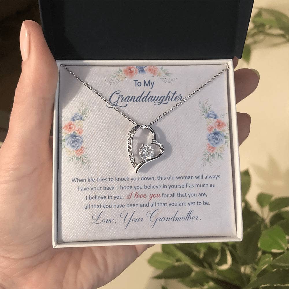 Alt text: "A hand holding a Personalized Granddaughter Necklace of Love in a box, featuring a heart-shaped pendant with a cubic zirconia stone. Adjustable chain length and luxurious packaging included. Perfect for special occasions. From Bespoke Necklace."