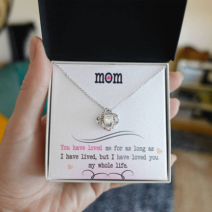 Alt text: "A hand holding a Personalized Mother Necklace - Love Knot Jewelry in a box, featuring a heart-shaped pendant adorned with cubic zirconia crystals."