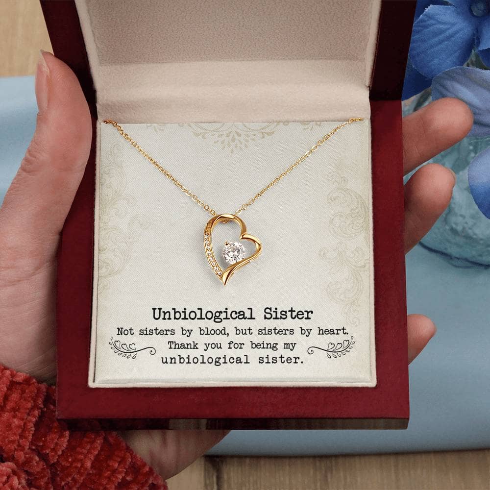 A hand holding a gold heart necklace with a diamond pendant in a box.