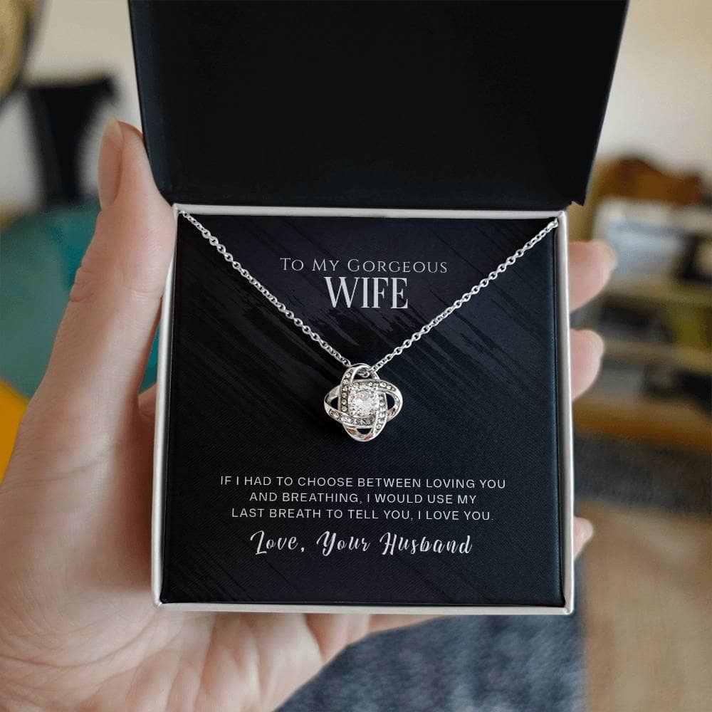 Alt text: "A hand holding a Love Knot Necklace in a box, a personalized gift for a cherished wife - a symbol of eternal affection and boundless love. The necklace features a heart-shaped pendant with dazzling cubic zirconia, adjustable chain options, and comes in a stylish mahogany-style box with an LED light."