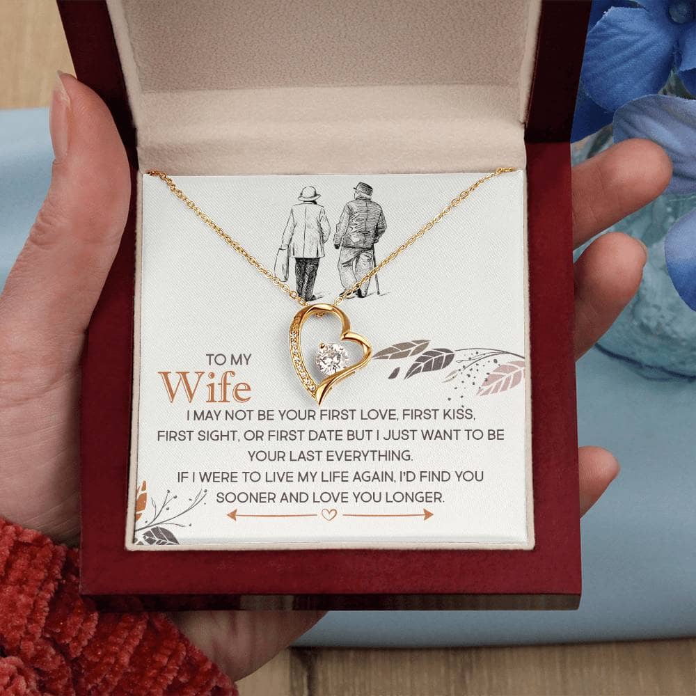 A hand holding a personalized wife necklace in a box. The necklace features a heart-shaped pendant with a diamond and a gold chain.