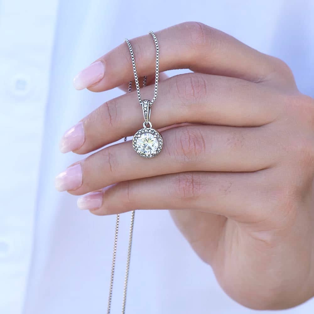 A hand holding a necklace with a shimmering cushion-cut cubic zirconia pendant, symbolizing everlasting love.