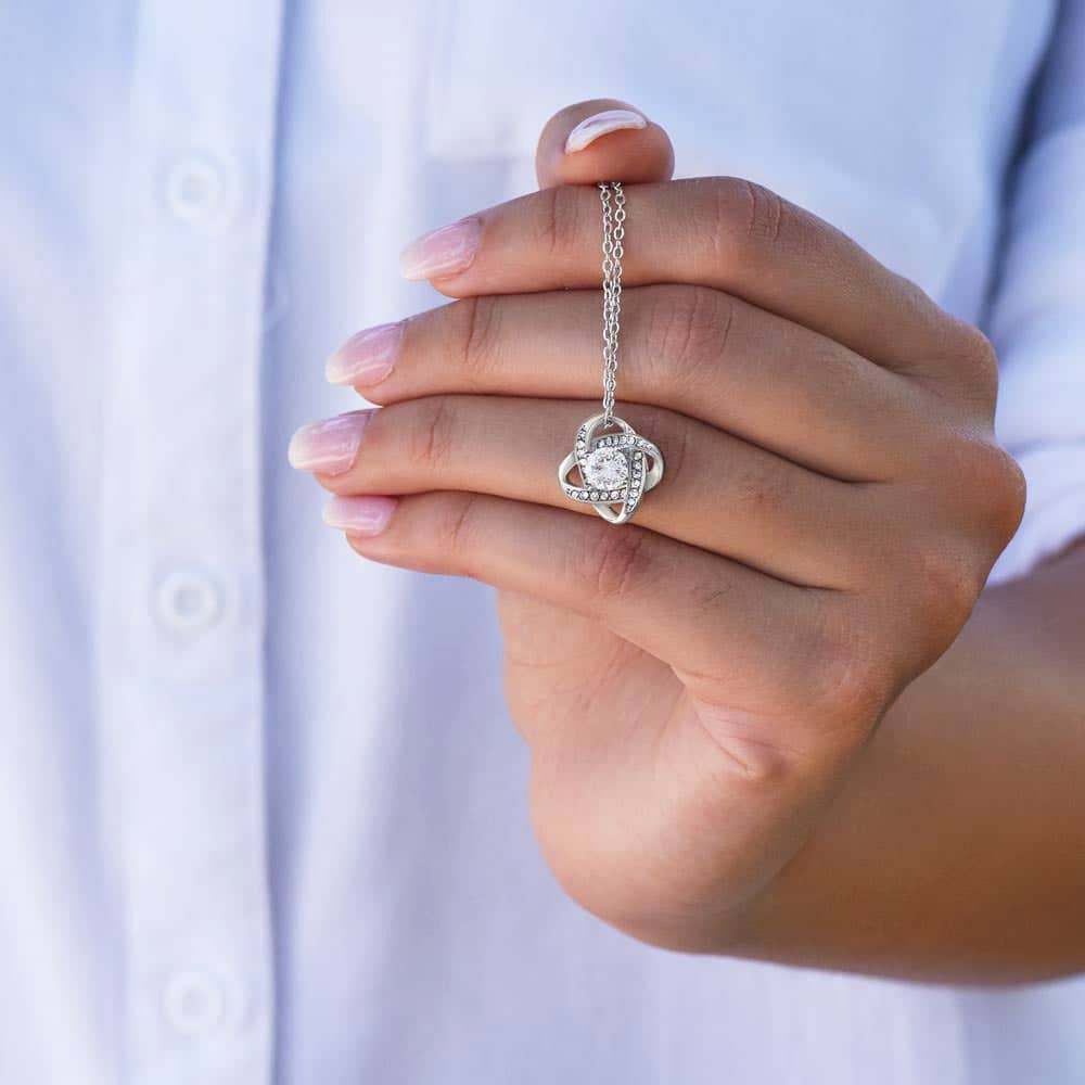 Alt text: "A hand holding a heart-shaped pendant necklace with a cushion-cut cubic zirconia, personalized with the message 'To My Wife'. Made of high-quality materials, this necklace is a symbol of endless love and cherished memories. From Bespoke Necklace."