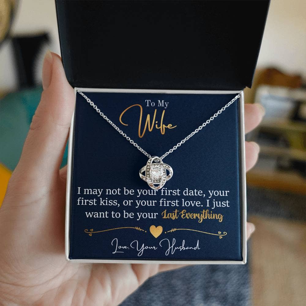 Alt text: "A hand holding the Personalized Wife Necklace: Love Knot Charm, a symbol of infinite love with a captivating heart-shaped pendant. Packaged in a stylish mahogany-style box with an LED light. Expertly crafted with premium cubic zirconia."