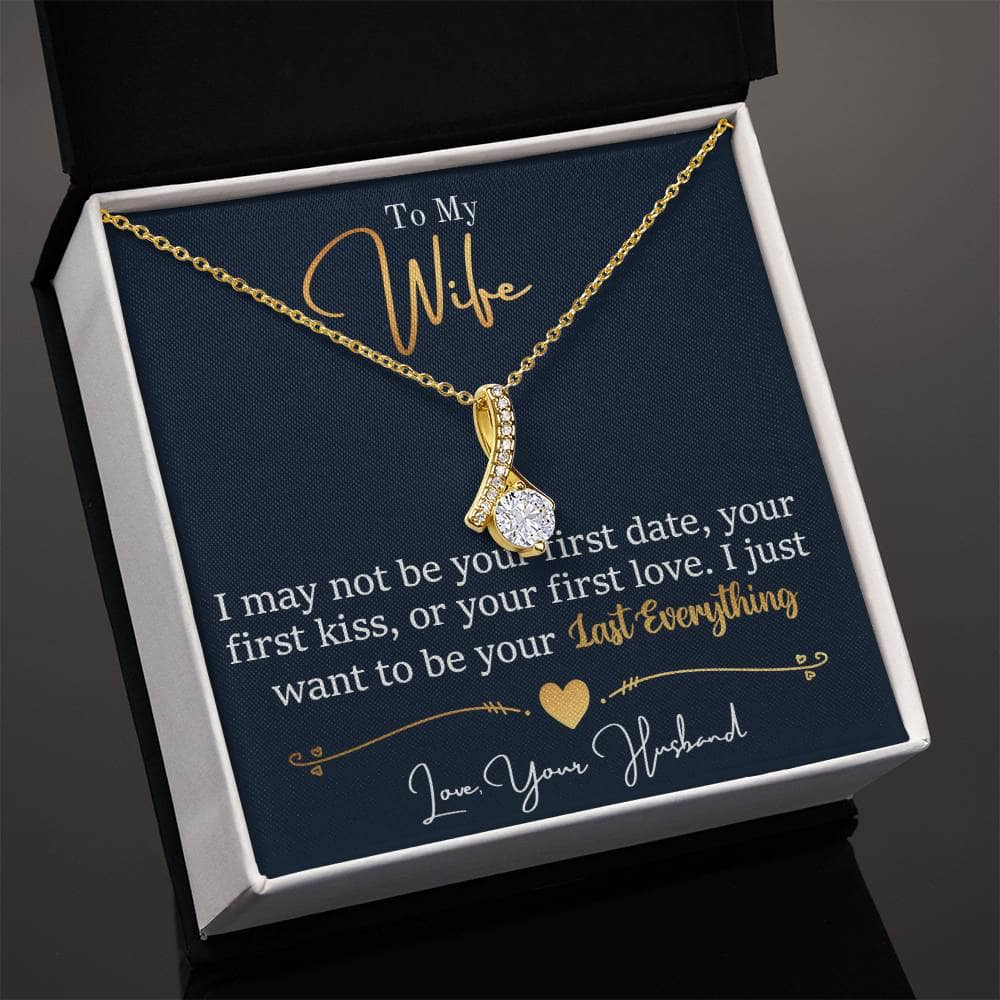 A gold necklace in a box, featuring a ribbon-shaped pendant adorned with a 7mm cubic zirconia. The Alluring Beauty necklace is a symbol of love and connection, perfect for a heartwarming gift.