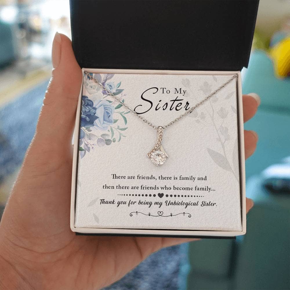 Alt text: "A hand holding the Alluring Beauty necklace in a box, featuring a ribbon-shaped pendant with a dazzling cubic zirconia. Perfect gift for a special someone. 14k white gold or 18k yellow gold finish. Adjustable length. Packaged in a soft touch box."