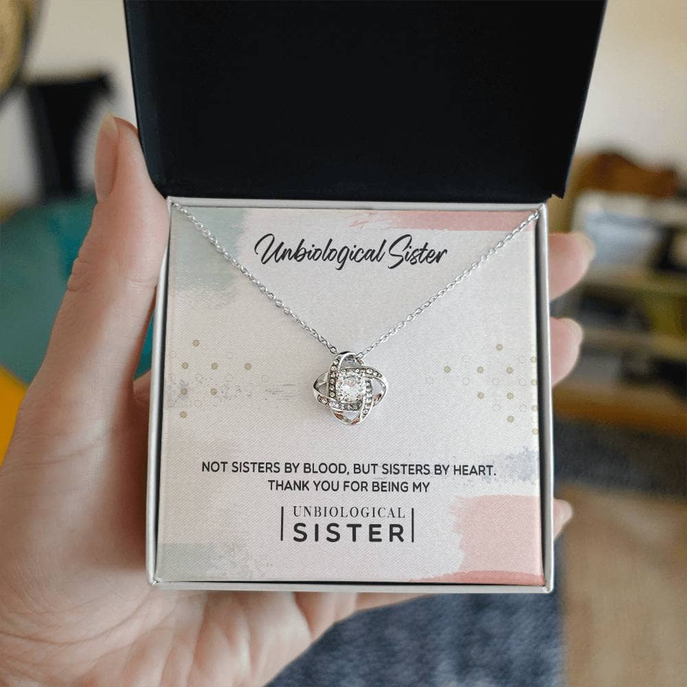 A hand holding a "Unbiological Sister" Custom Love Knot Pendant in a box with LED lighting.